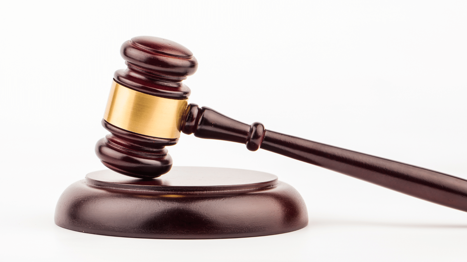 A wooden judge’s gavel with a gold band rests on a matching sound block against a white background.