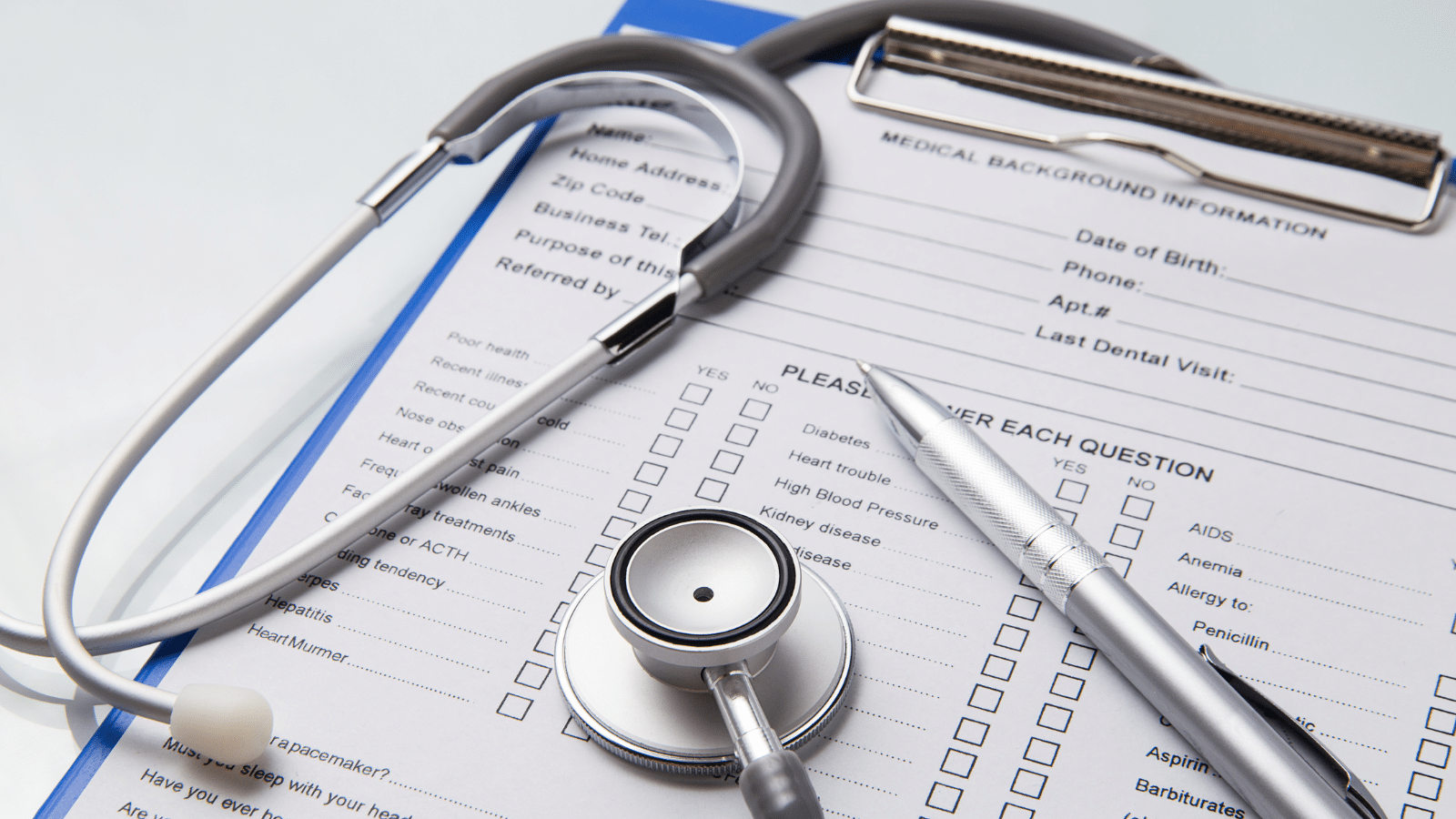 A stethoscope and pen rest on a clipboard holding a medical background information form, with checkboxes and fields for personal and health details visible.