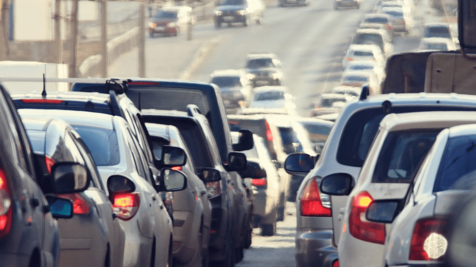Heavy traffic jam on a multi-lane road with cars lined up closely, their brake lights on, stretching into the distance under daylight.