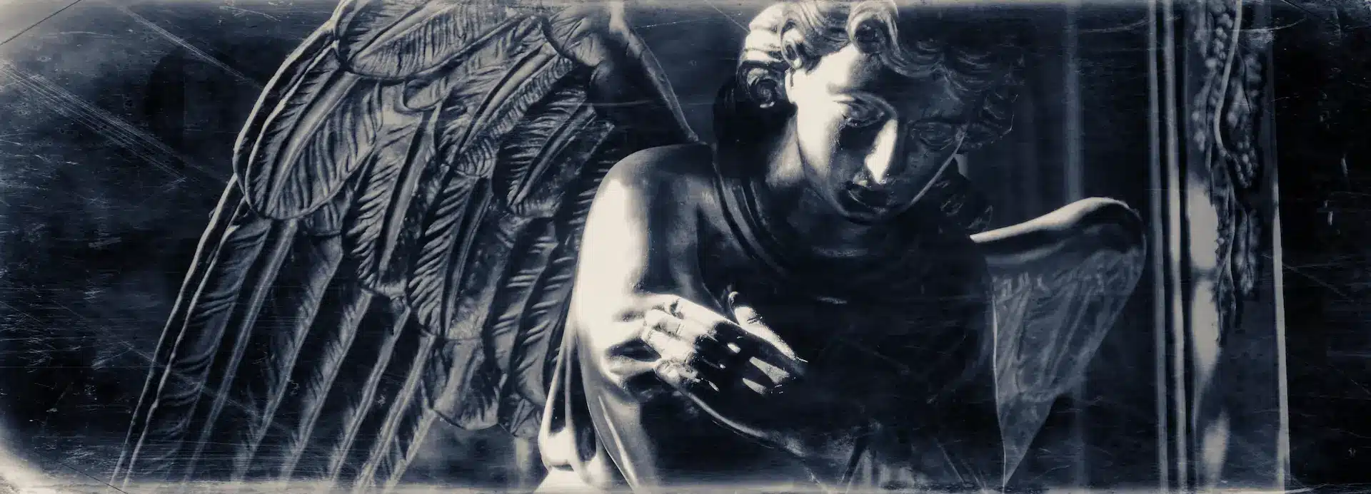 A close-up of a dark, weathered angel statue with detailed wings, gazing downward with a somber expression. The image has a vintage, distressed effect and is rendered in black and white.