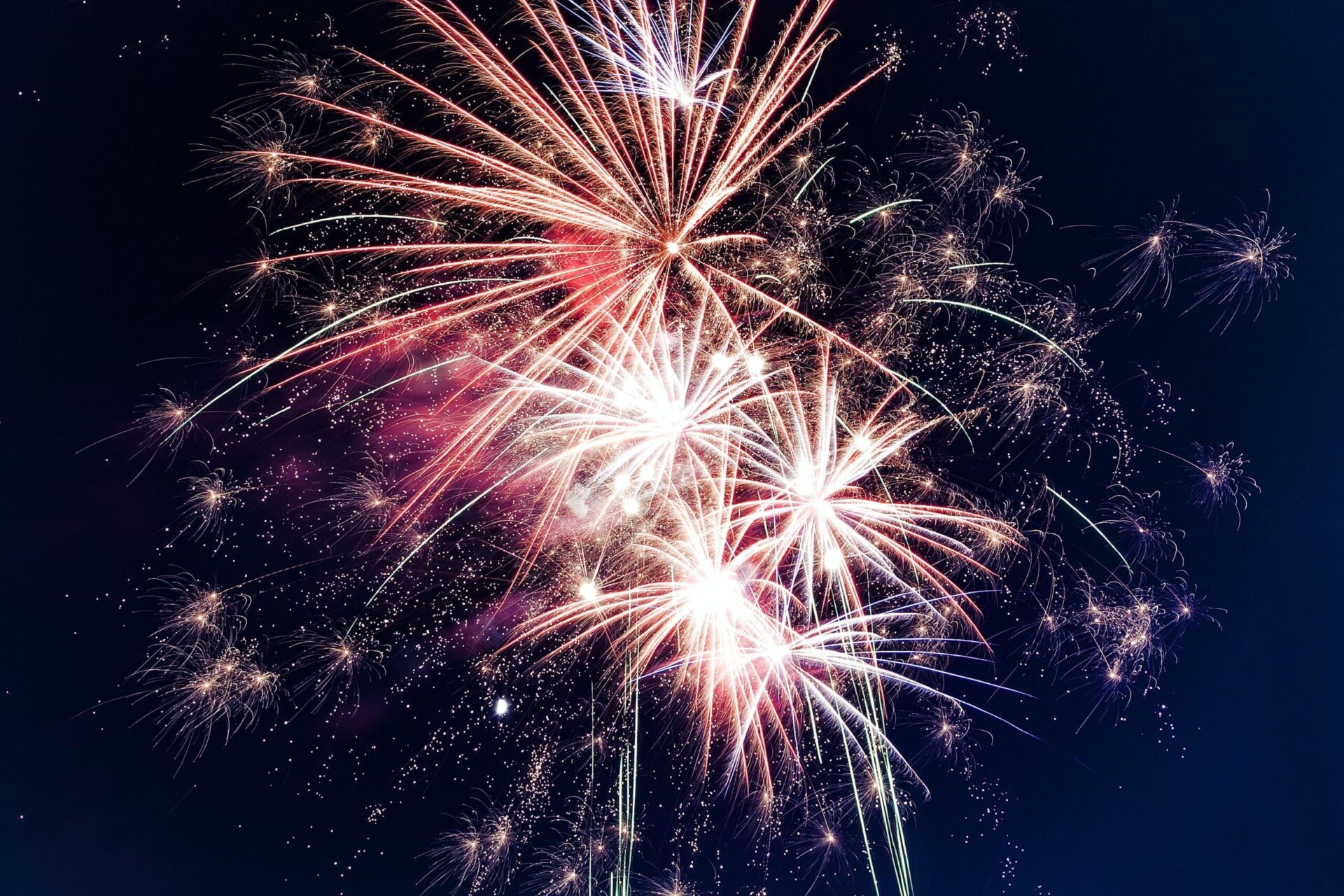 Colorful fireworks burst in the night sky, creating bright streaks and sparkling patterns against a dark blue background.