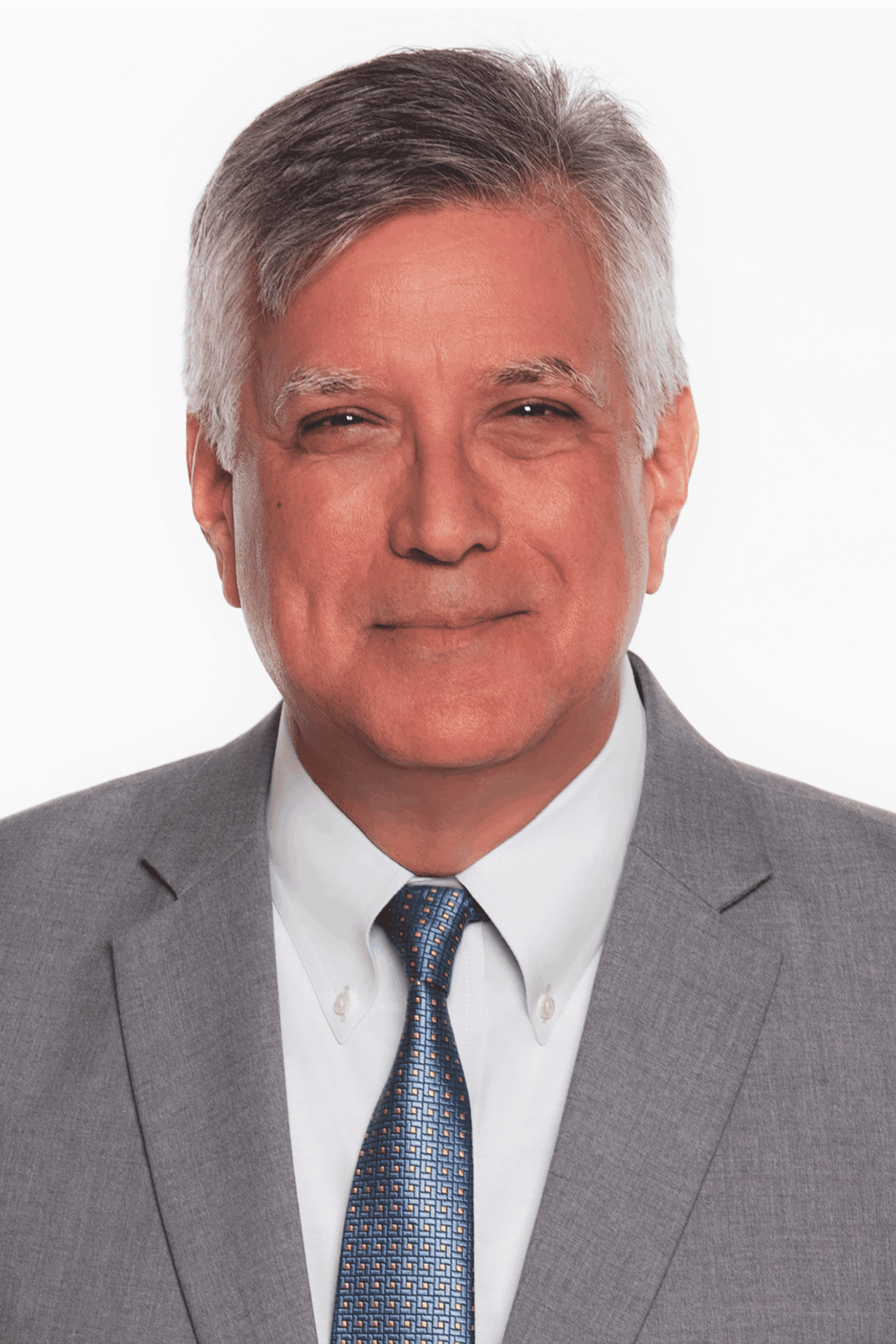 A middle-aged man with short gray hair, wearing a light gray suit, white dress shirt, and blue patterned tie, smiles slightly in a professional headshot against a plain white background.