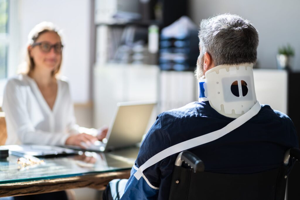 a woman in front of a laptop looking at a man who has on a neck brace and arm aling