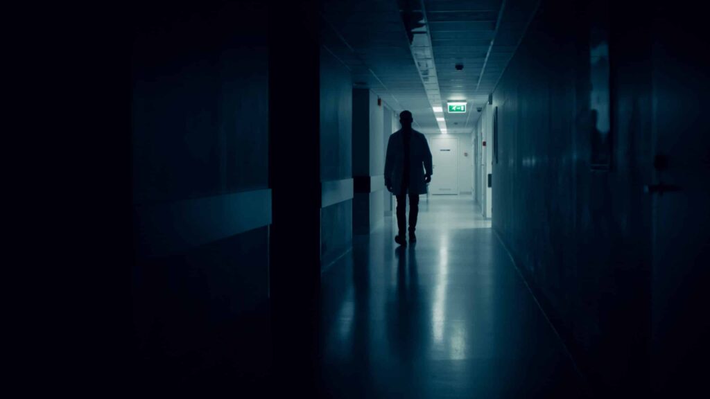 Medical Doctor Silhouette Walks in Dark Part of the Hospital Corridor.