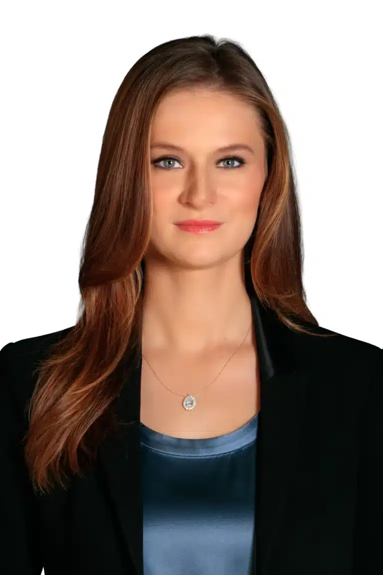 Kayla Ferrel with long brown hair wearing a black blazer over a blue top, accessorized with a pendant necklace, poses against a plain white background.