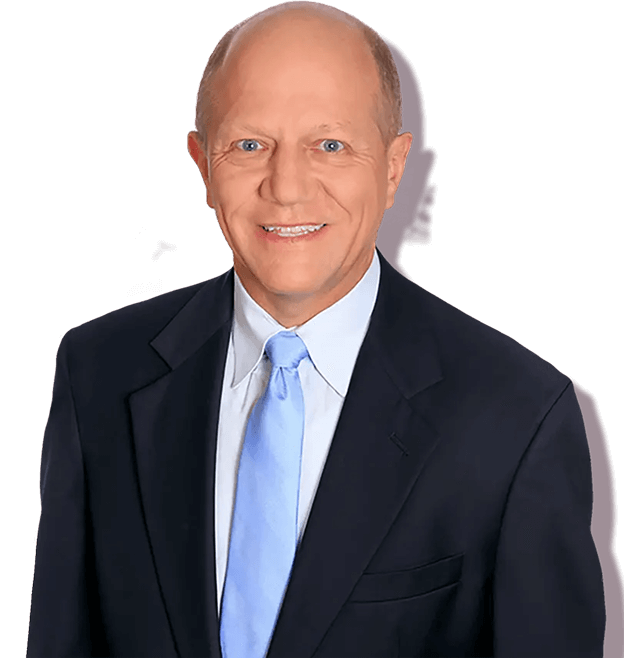 A smiling, middle-aged man with short, light hair, wearing a dark suit, white shirt, and light blue tie, standing against a plain white background.
