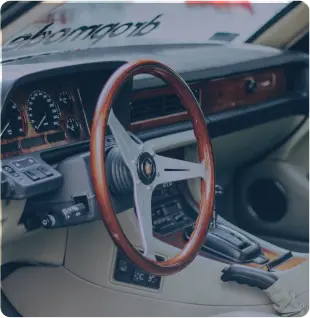Vintage car interior featuring a wooden steering wheel, analog gauges, and beige leather seats, with classic dashboard controls and a gear shifter visible.