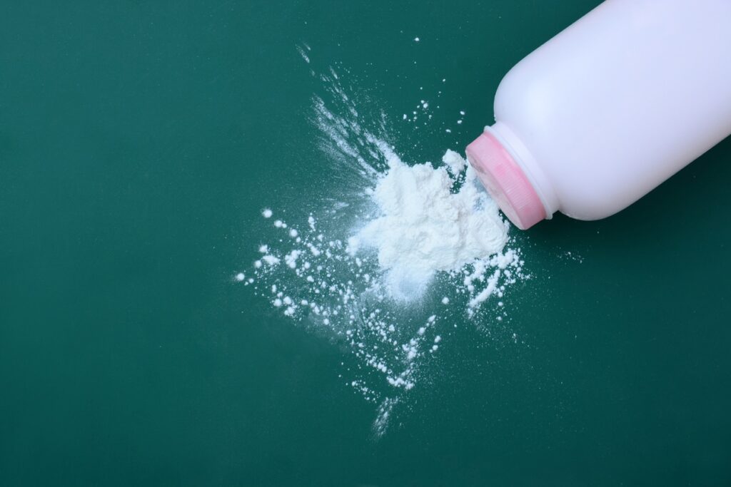 A white plastic bottle with a pink cap is tipped over, spilling white powder onto a green surface.