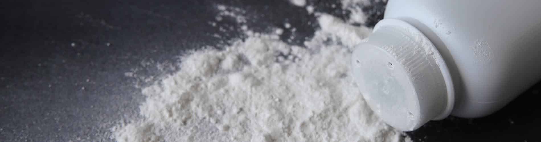 A white plastic bottle of talcum powder lies on its side, with powder spilled onto a dark surface.