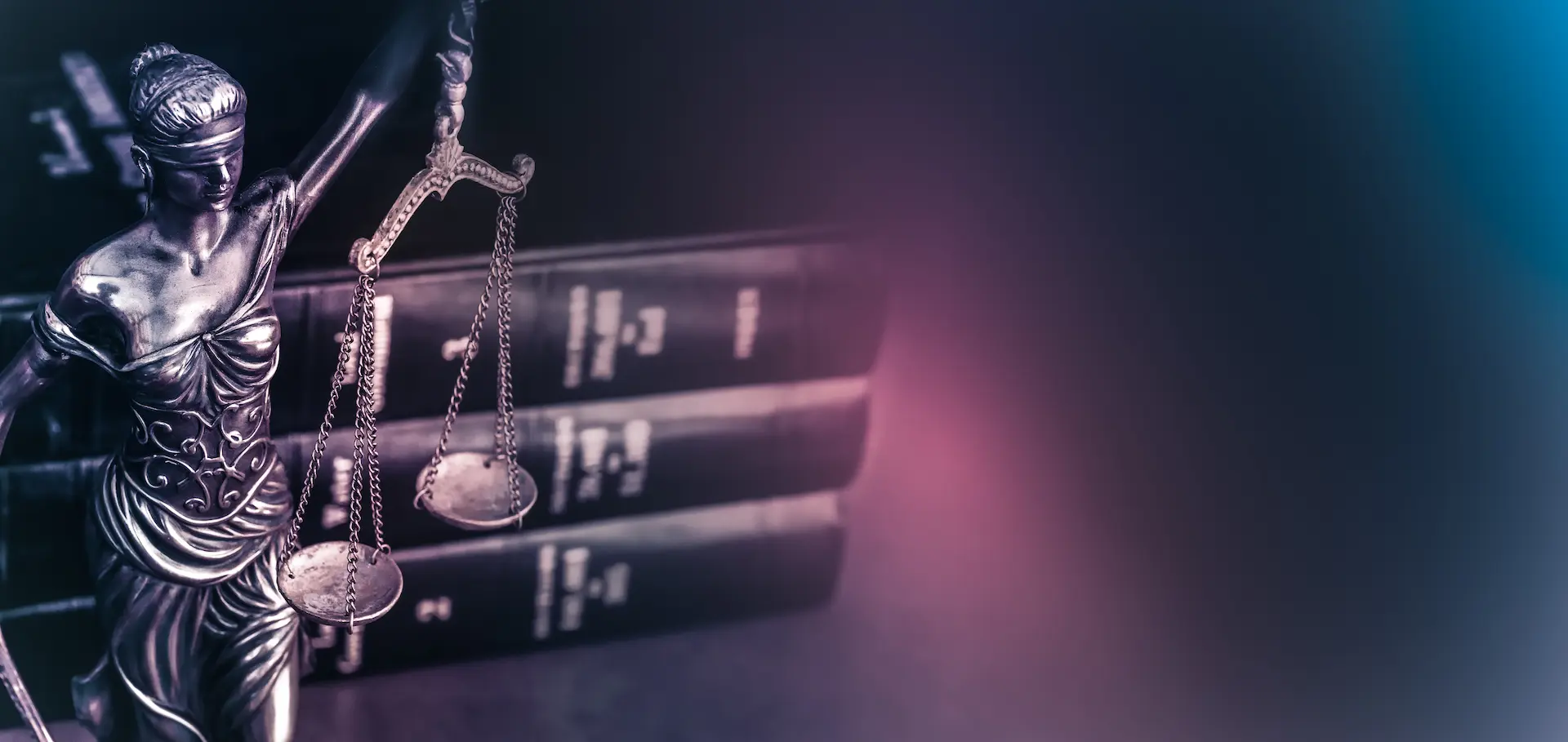 A metallic statue of Lady Justice holding balanced scales stands in front of three stacked law books, with a dark, blurred background featuring purple and blue highlights.