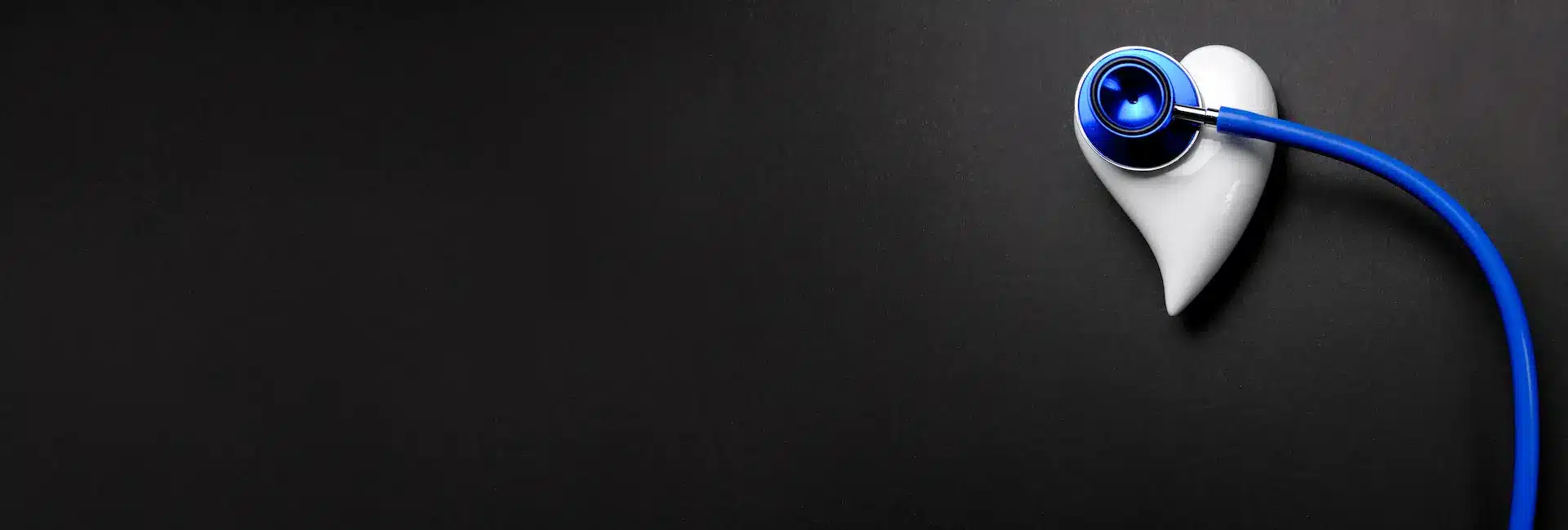 A blue stethoscope rests on a white heart-shaped object against a black background, symbolizing heart health and medical care.